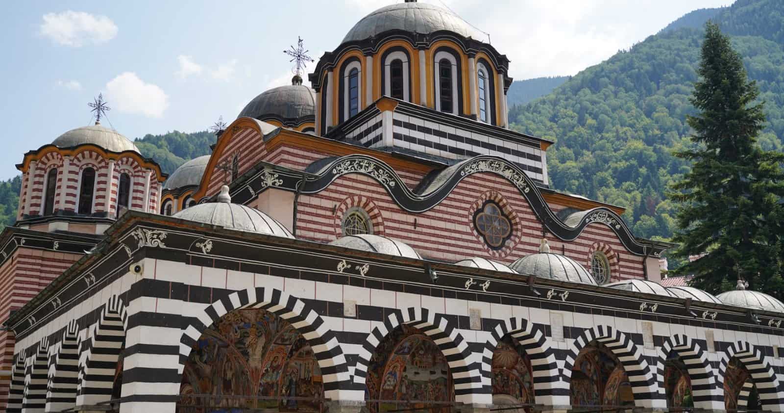 The striped arcades and domes of Rila Monastery below the forested Rila mountains, Bulgaria