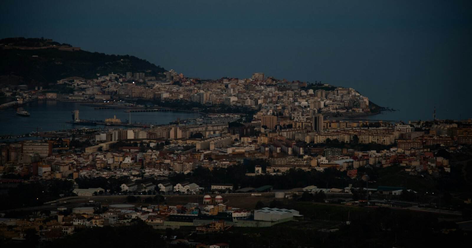 Ceuta seen from the sea at dusk, with the city on the isthmus and Monte Hacho behind