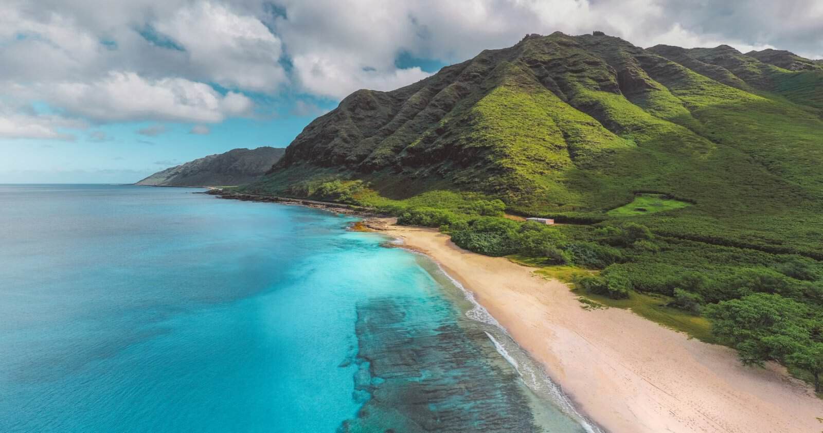 Aerial view of a reef-fringed Hawaiian coastline with green mountains