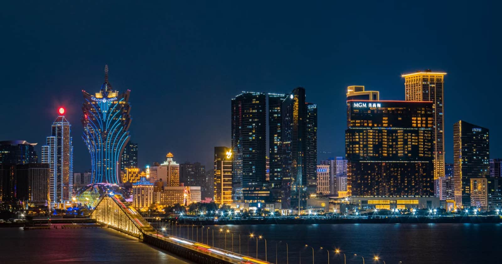 Macau skyline at night with illuminated casino towers and a lit bridge over the water
